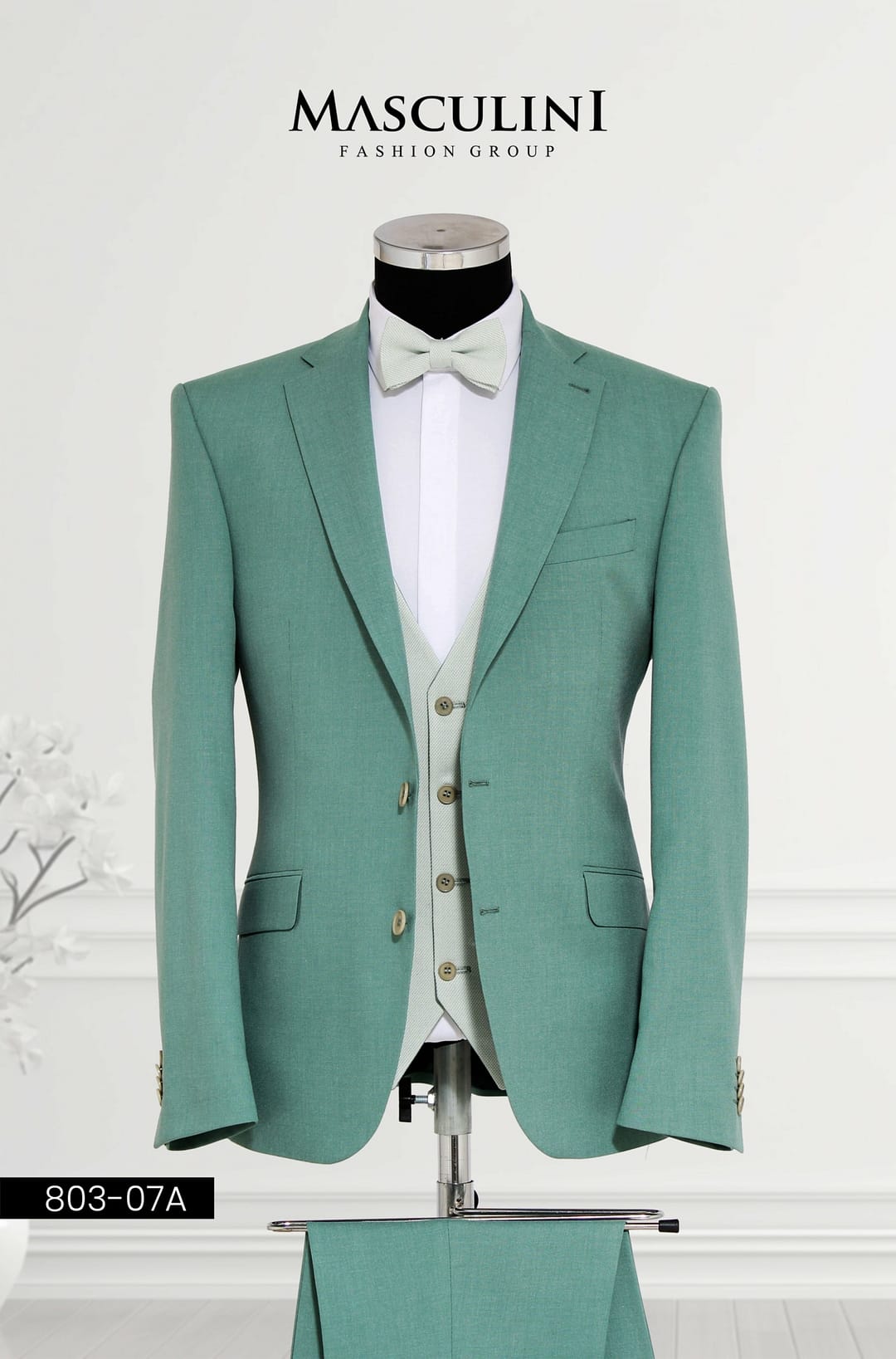 803-07A Ein mintgrüner Masculini 803-07A Anzug mit Weste und Fliege wird auf einer Schaufensterpuppe vor weißem Hintergrund präsentiert - ideal für einzigartige Brautmoden und zur Aufwertung jedes Hochzeitskleid-Ensembles.